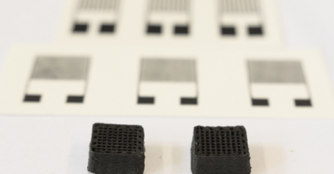 Neuartiger Werkstoff für gedruckte Schaltungen: Zwei Testquader von einem Zentimeter Breite aus dem 3D-Drucker. Im Hintergrund sieht man die gedruckten elektronischen Sensoren. Bild: Empa